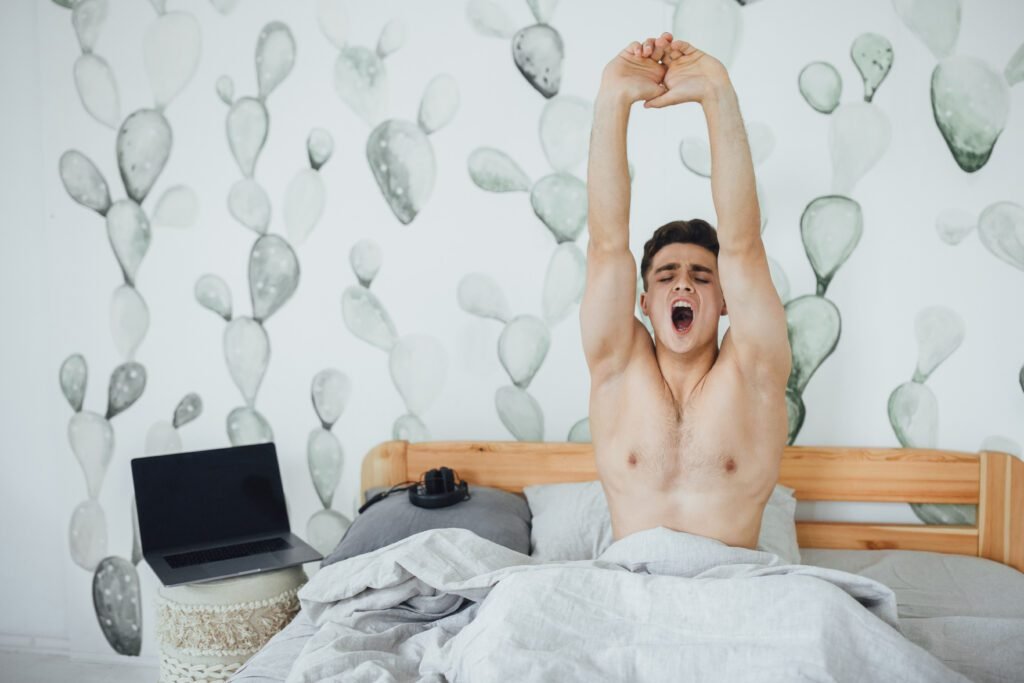 Young man stretching in bed after waking up – represents morning energy and male health