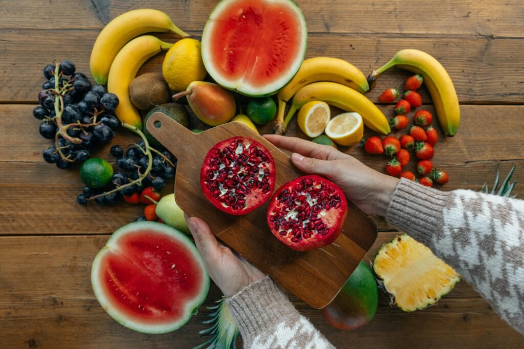 	A person holding sliced pomegranate with fruits like watermelon and banana